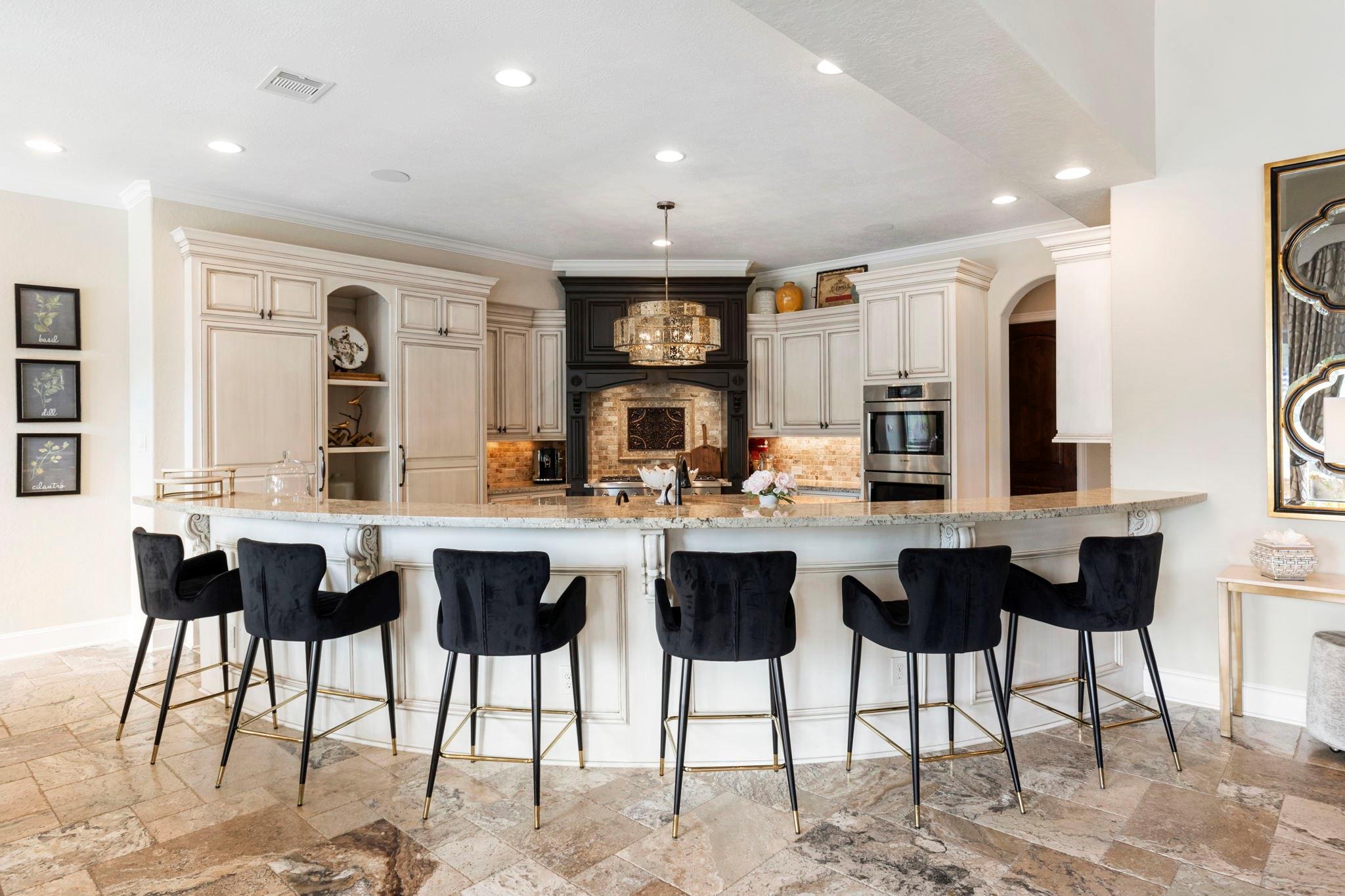 Kitchen with a curved island, six dark bar stools, cream cabinets, and a prominent dark wood range hood.
