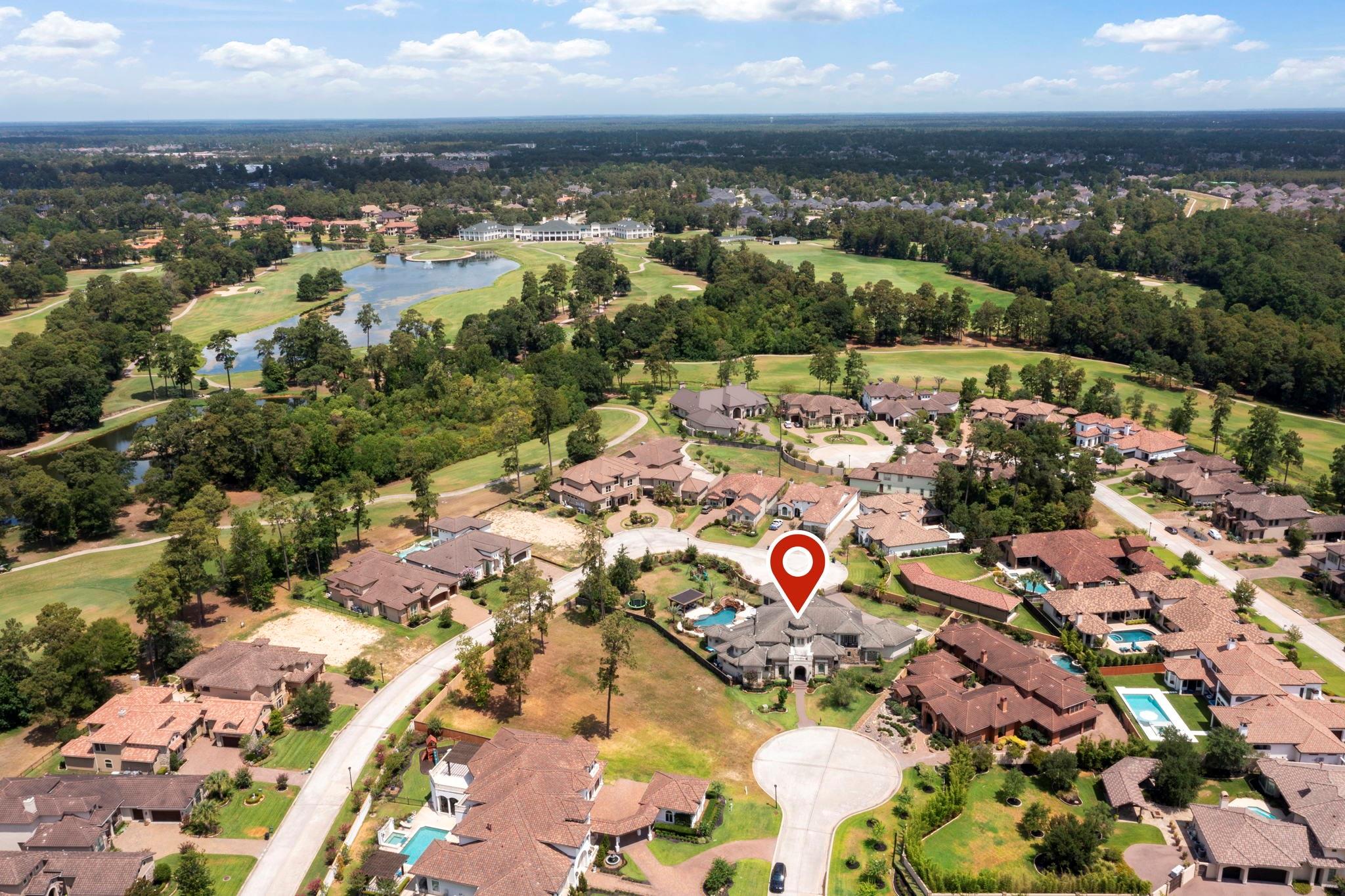 Aerial view of a home marked among neighborhood houses, beside a golf course with ponds and a clubhouse.