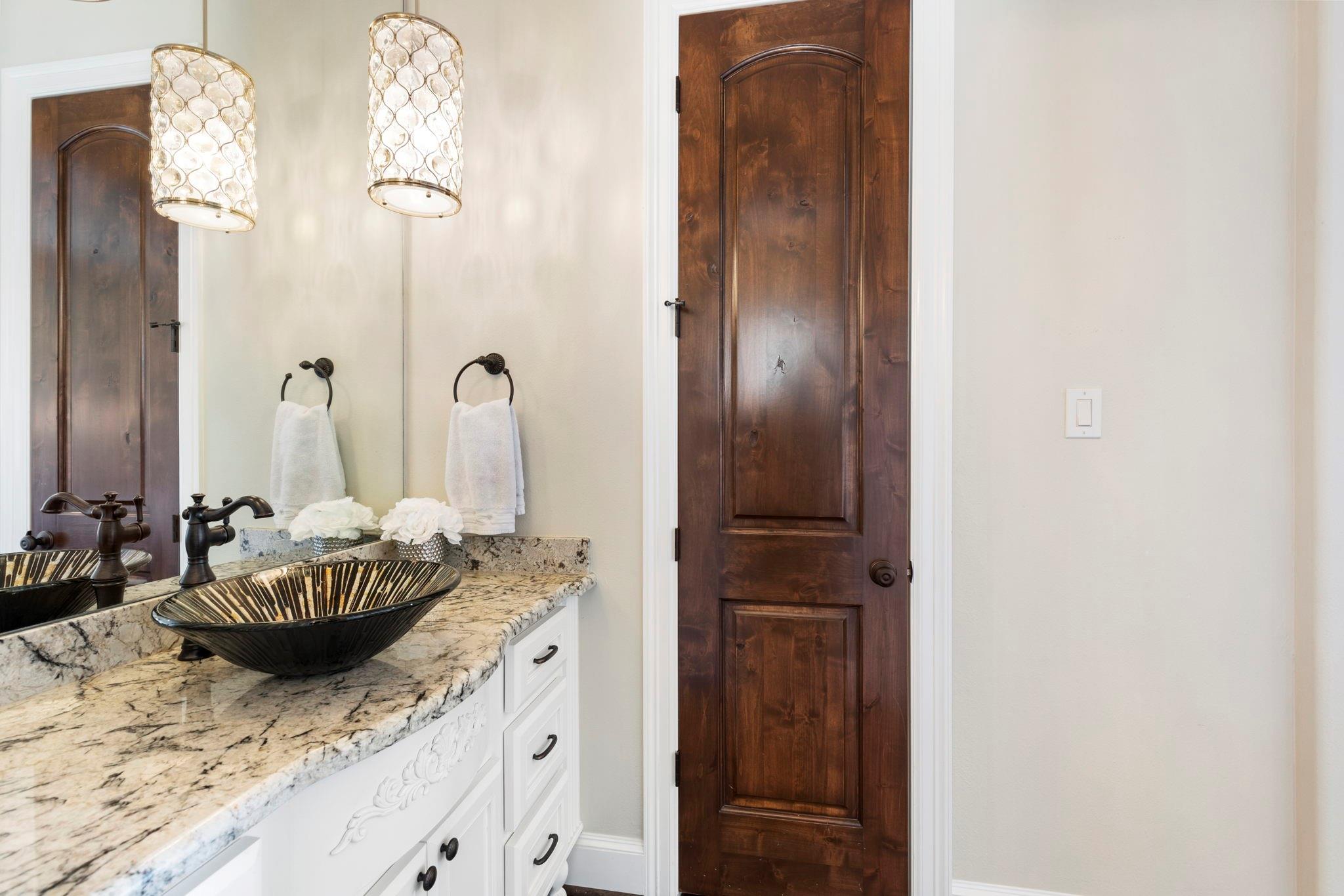 Bathroom vanity with a striped vessel sink, stone countertop, and dark wood door.