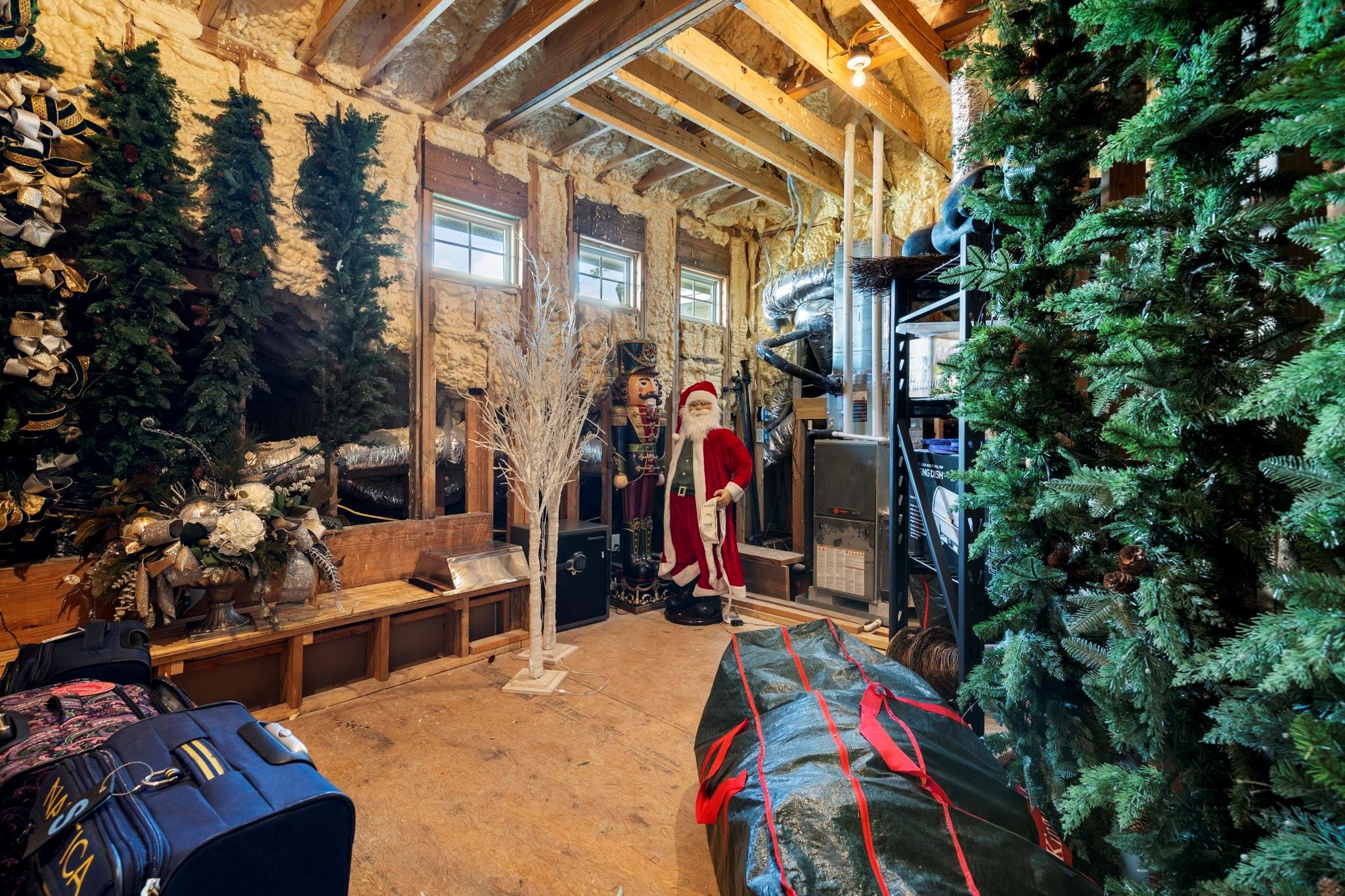 Attic storage area with exposed framing, HVAC equipment, Christmas trees, and luggage.