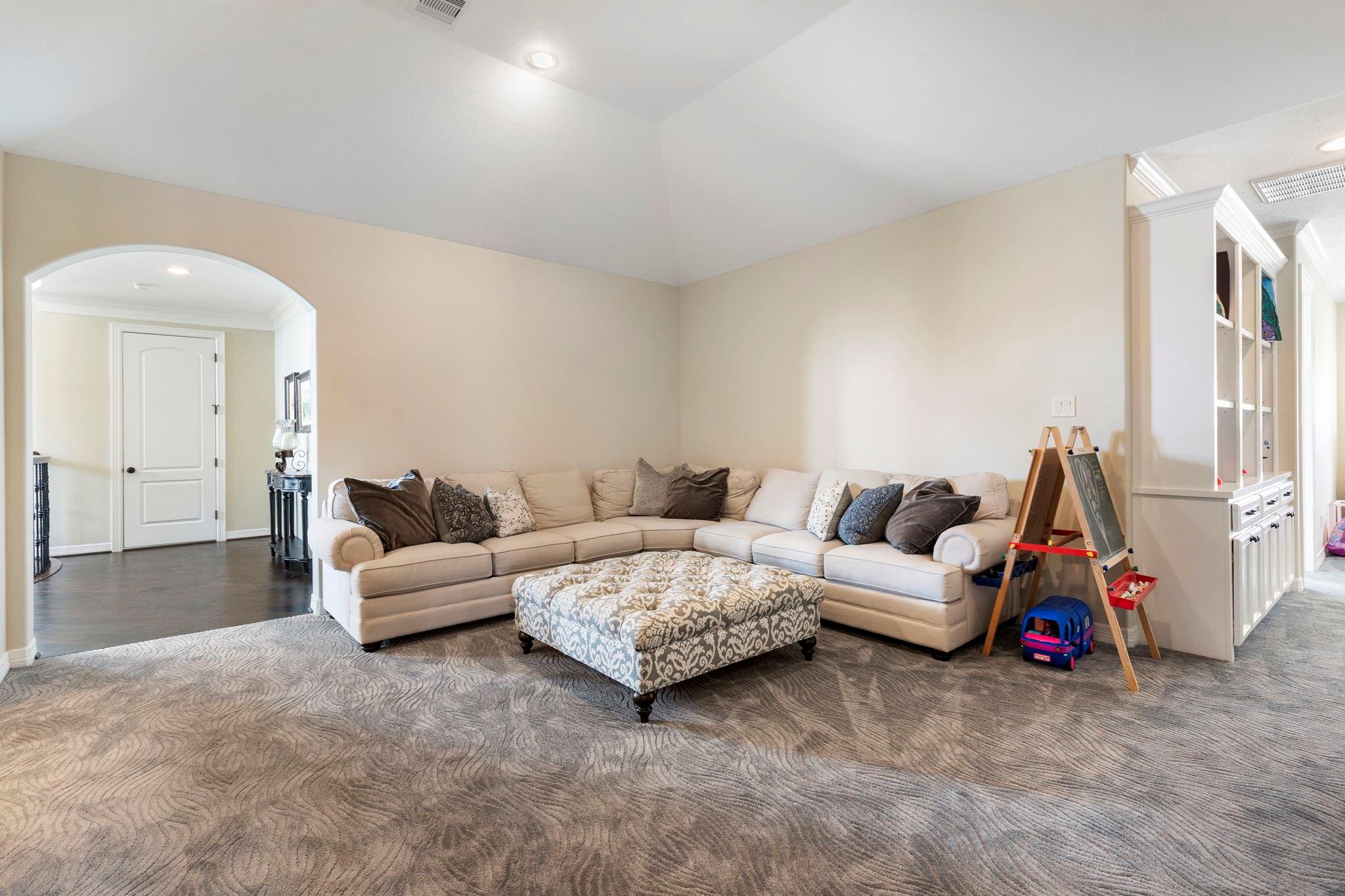 Living room with a beige sectional, patterned ottoman, arched doorway, and built-in cabinetry.