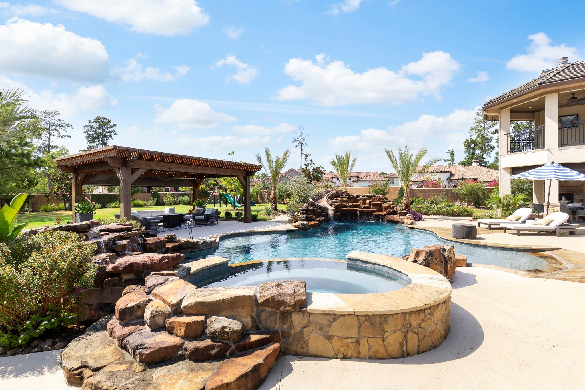 Backyard pool and raised stone spa with a rock waterfall, pergola, and covered patio.