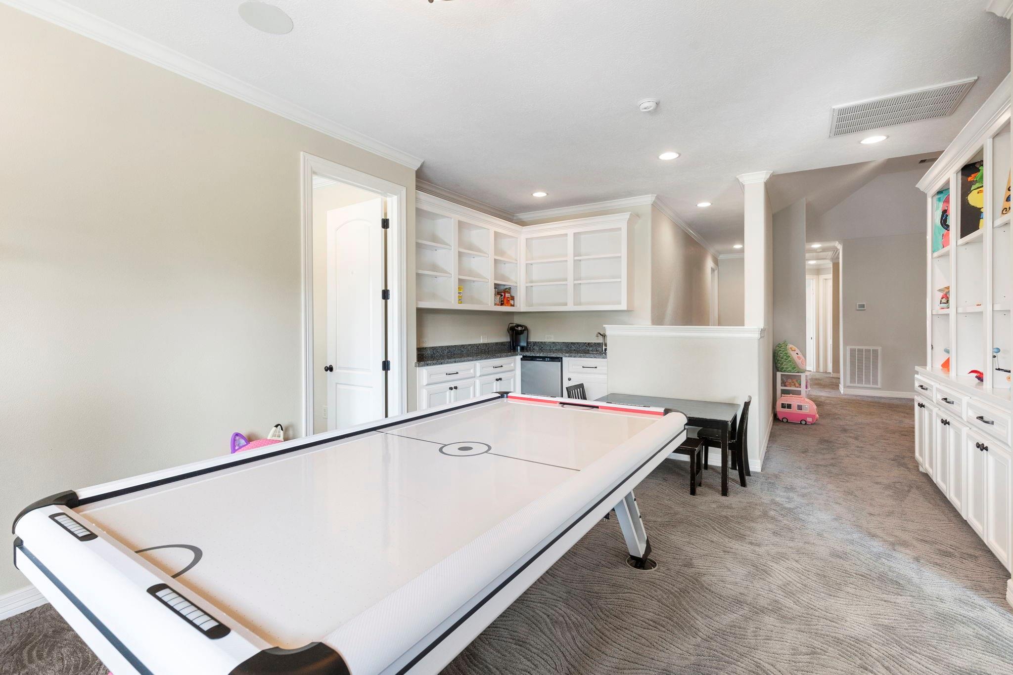 Game room with a large air hockey table, built-in white cabinets, and a small dining area.