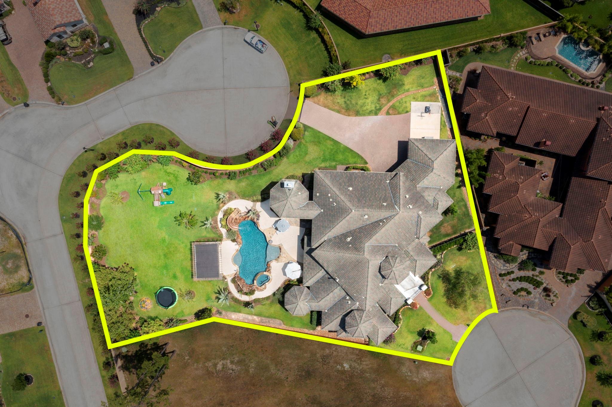 Aerial view of a home with a pool, large lawn, and play equipment inside a yellow property outline.