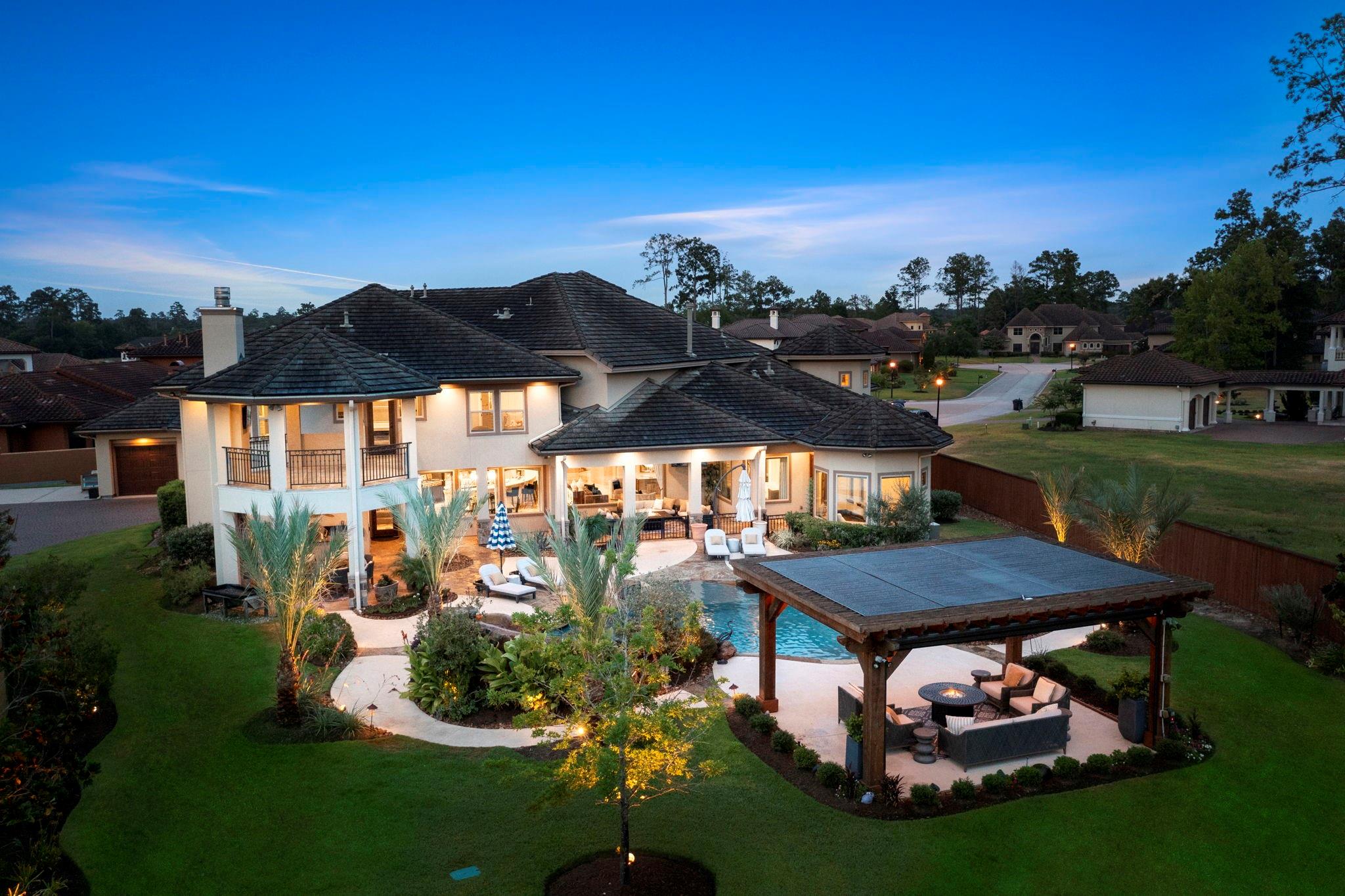 Home’s rear exterior at dusk, with a swimming pool, landscaped yard, and covered patio seating.