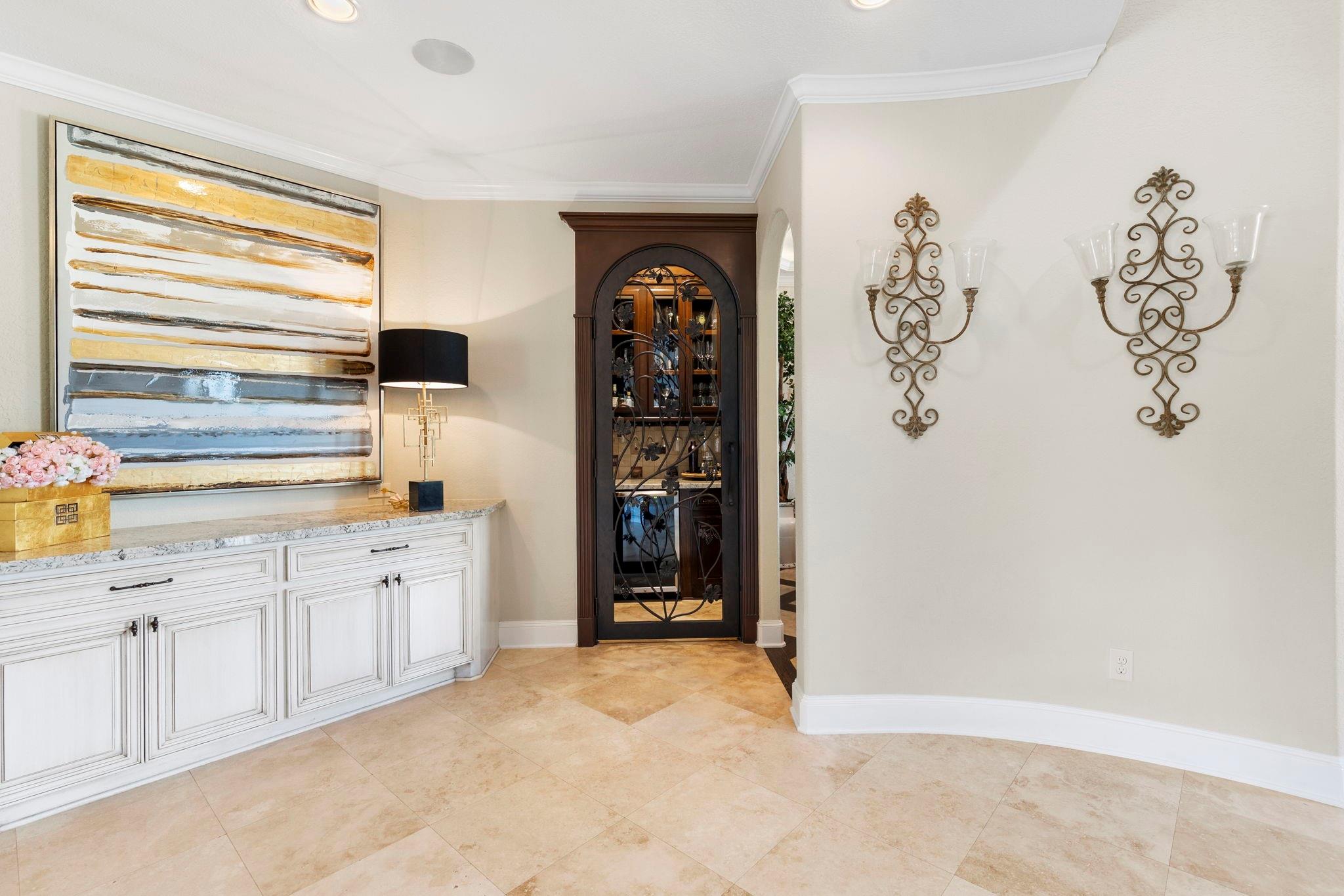 Furnished entry hall with tan tile floors, white cabinetry, abstract artwork, and an arched glass cabinet door.