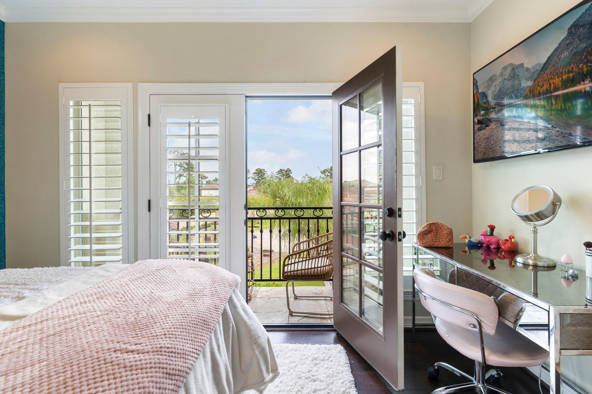 Bedroom with an open balcony door, plantation shutters, and a glass-topped vanity.