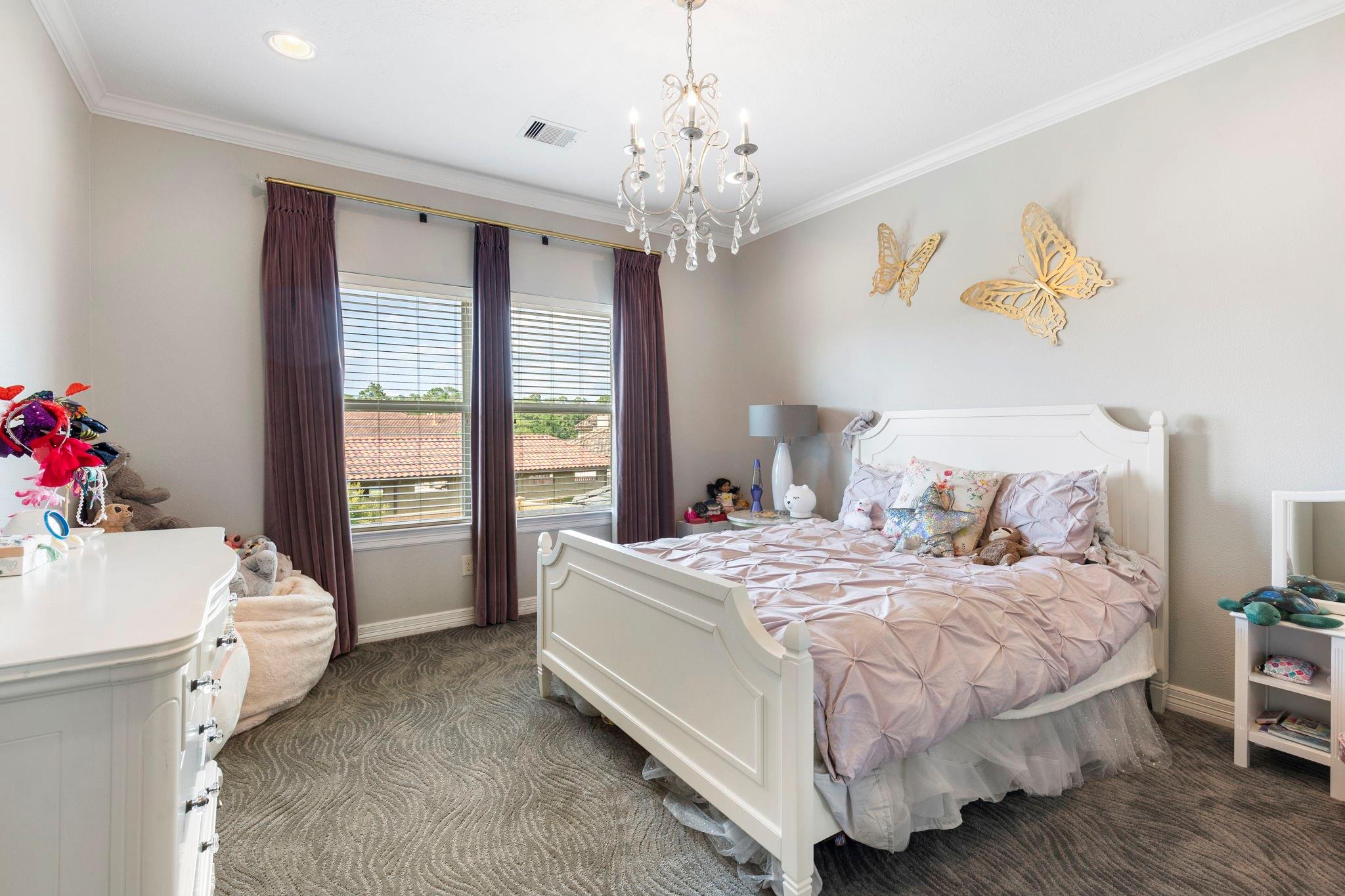 Bedroom with a white bed, pale pink bedding, crystal chandelier, and gold butterfly wall decor.