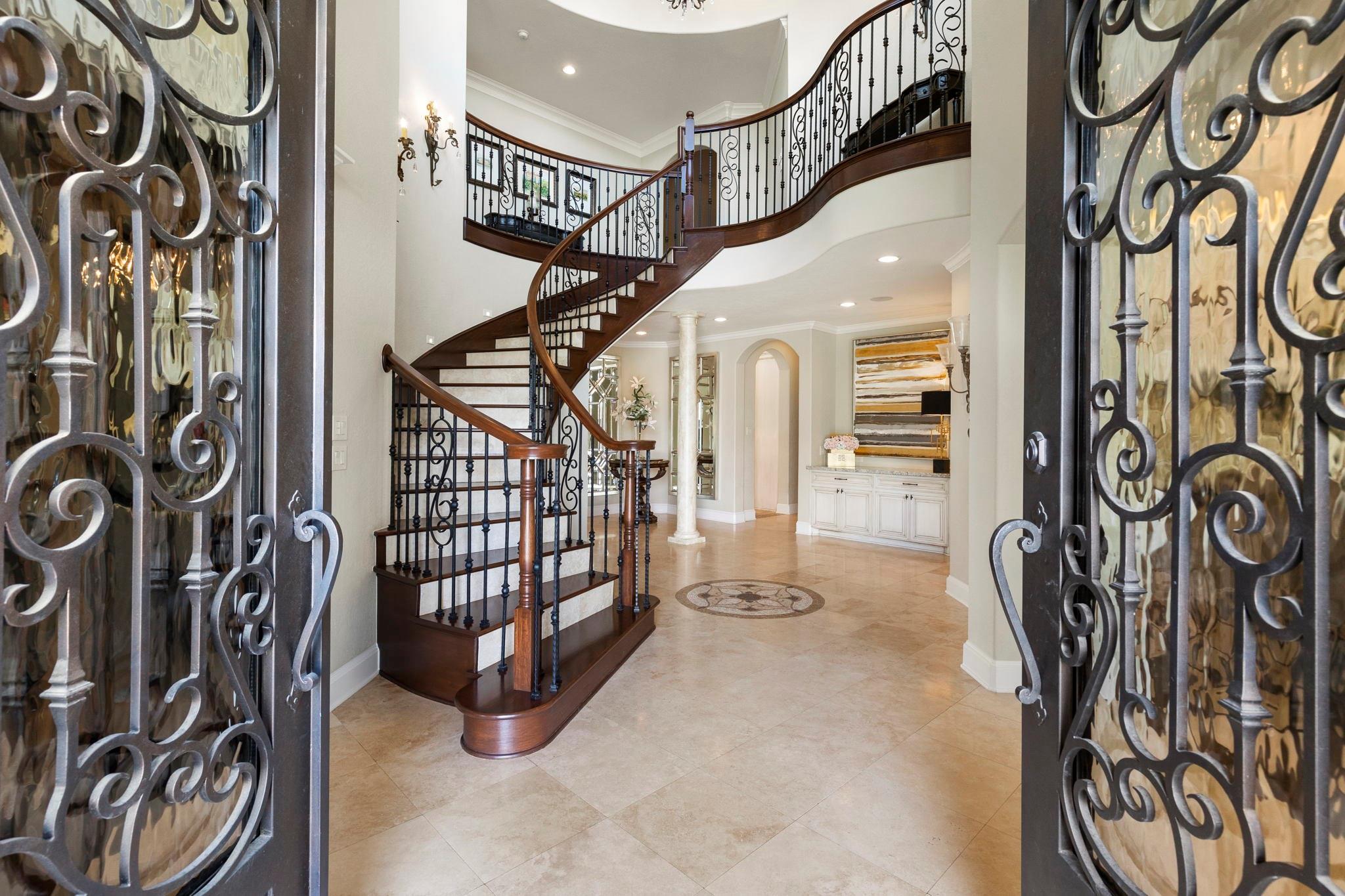 Two-story foyer with a sweeping curved staircase and ornate iron entry doors.