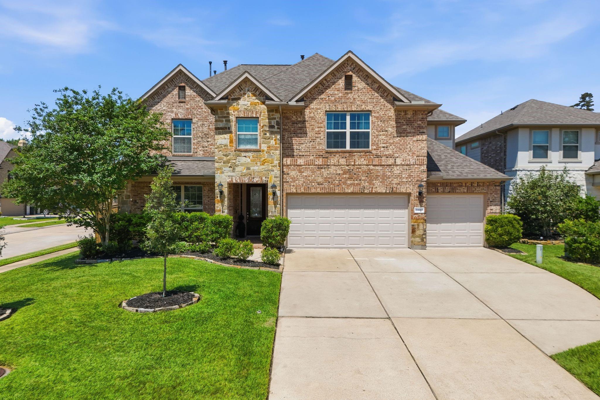 Two-story brick house with stone accents, three-car garage, landscaped lawn, and wide driveway.