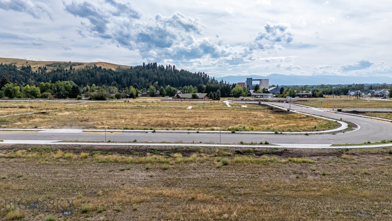 Vacant land beside a curving paved road, with wooded hills and distant mountains beyond.