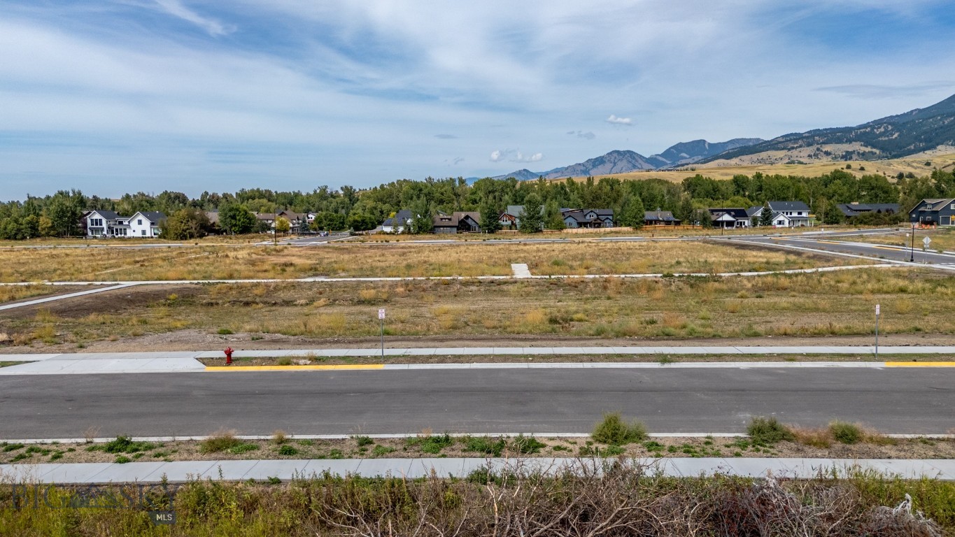 Vacant subdivision lot with paved streets, neighboring homes, and mountains in the distance.
