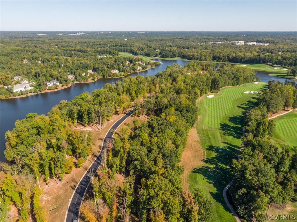Aerial view of a golf course and winding waterway among wooded homes and a curving road.