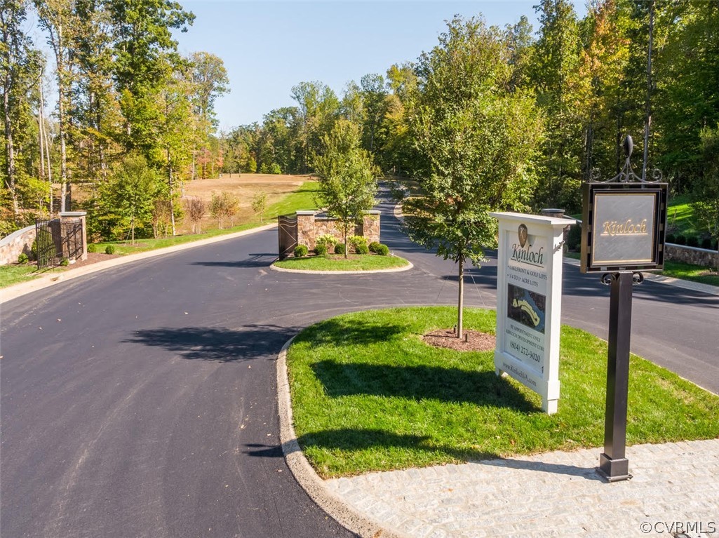 Kinloch community entrance with ornamental signs, stone walls, and a tree-lined paved road.