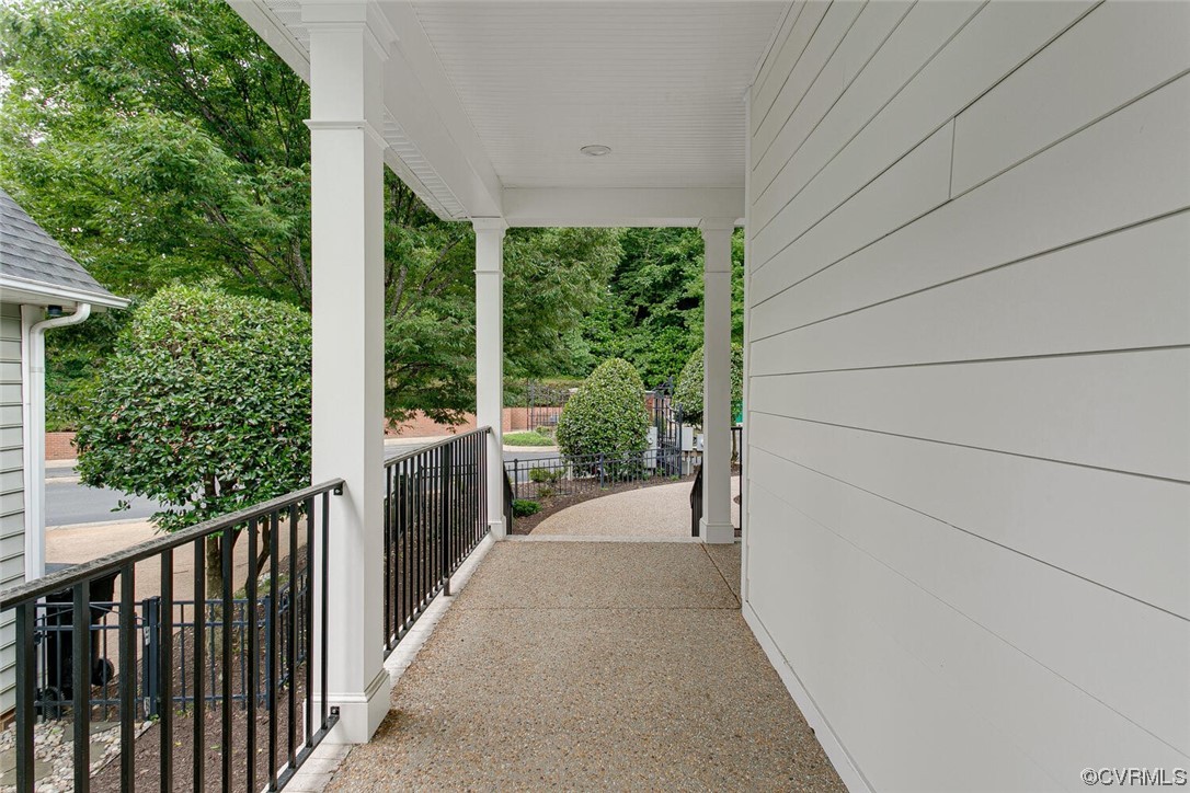 Covered porch walkway with black railings and leafy landscaping beside white siding.