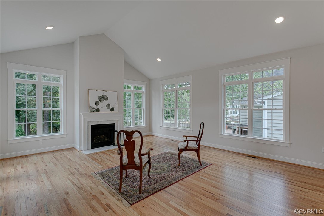 Living room with a fireplace, tall windows, hardwood floors, and two chairs on a patterned rug.