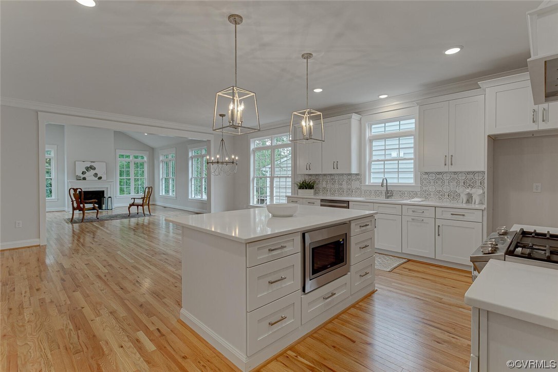 White kitchen with a large island, patterned backsplash, hardwood floors, and an adjoining sitting area.