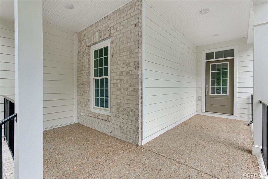 Covered front porch with a taupe glass-paneled door and pale brick window wall.