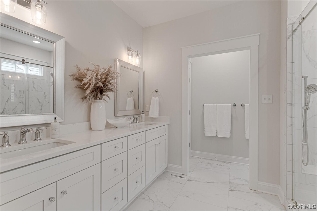 Bathroom with a long white double-sink vanity, marble-look surfaces, and a glass shower.