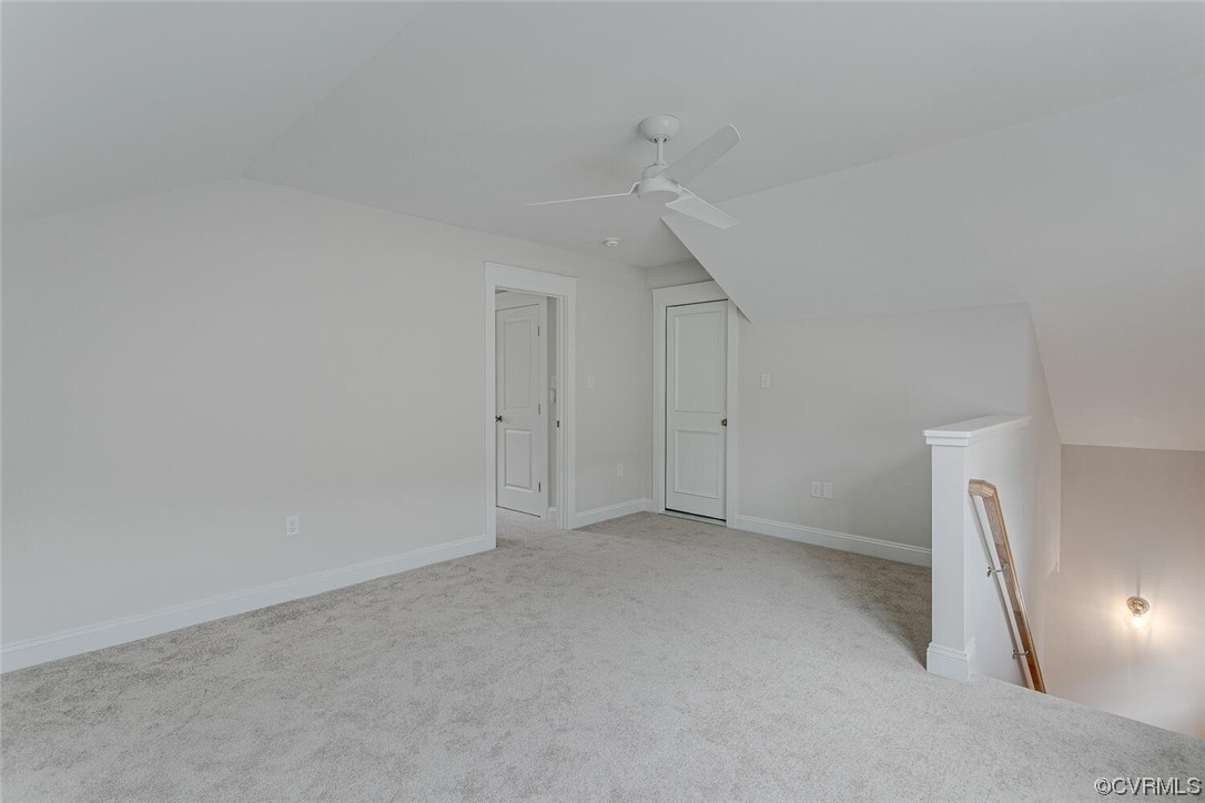Empty carpeted loft with a ceiling fan, sloped ceiling, and open stairwell.
