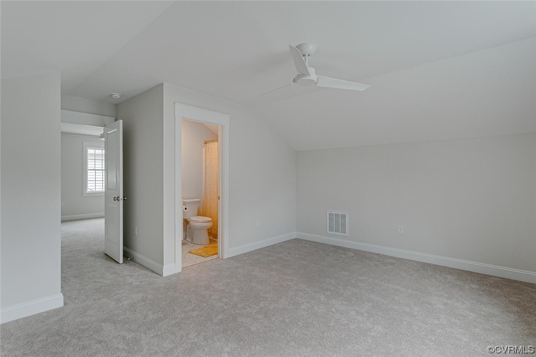 Empty carpeted bedroom with a ceiling fan and open doorways to a bathroom and adjoining room.