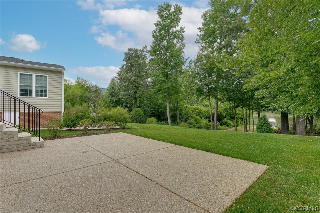 Concrete patio beside the home overlooks a lawn, mature trees, and a glimpse of water.