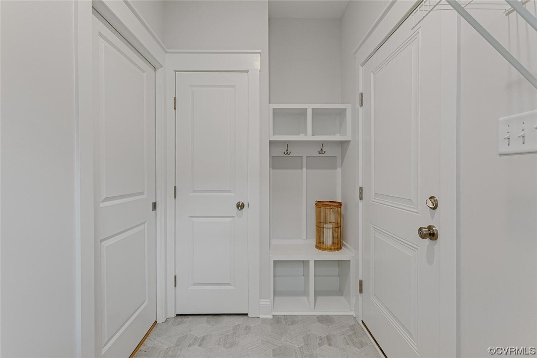 Mudroom with white built-in cubbies and hooks, a bench, paneled doors, and patterned gray tile.