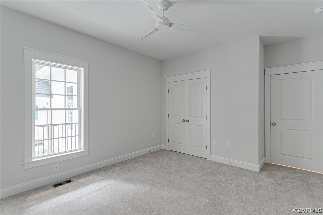 Empty bedroom with gray carpet, a large window, ceiling fan, and double-door closet.