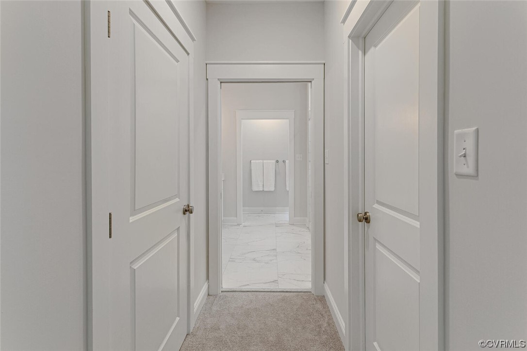 Hallway leading to a bathroom with marble-look tile flooring and white paneled doors.