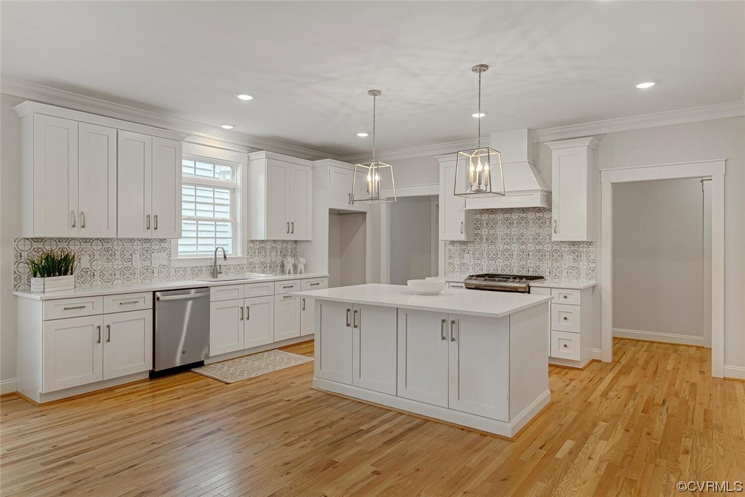 Kitchen with white cabinetry, a large island, patterned tile backsplash, and hardwood floors.