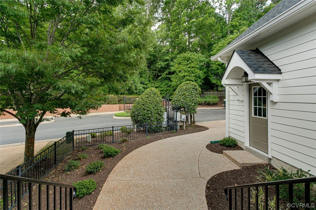 Home entrance with a curved walkway, landscaped beds, and black metal fencing.