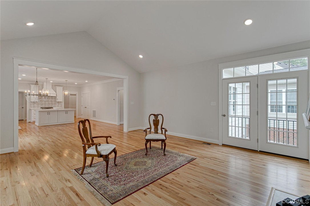 Open living room with hardwood floors, two chairs on a patterned rug, and French doors beside tall windows.