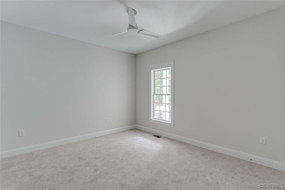 Empty carpeted room with a tall window and modern ceiling fan.
