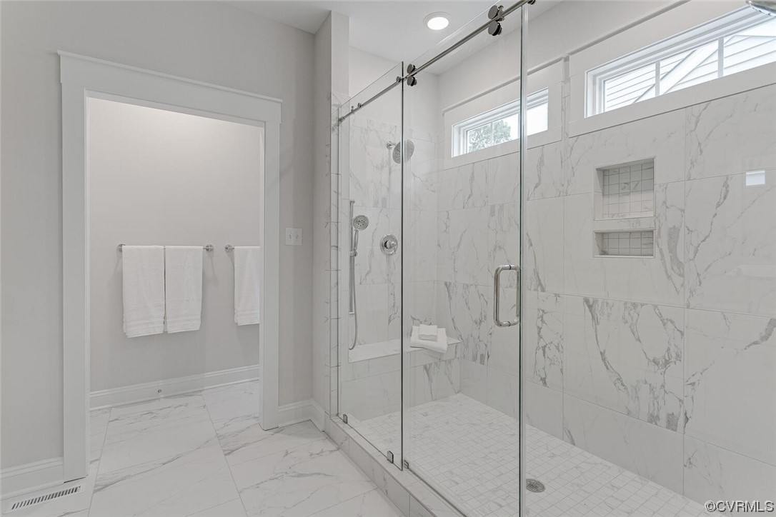 Bathroom with a glass walk-in shower, marble-pattern tile, built-in niches, and high windows.