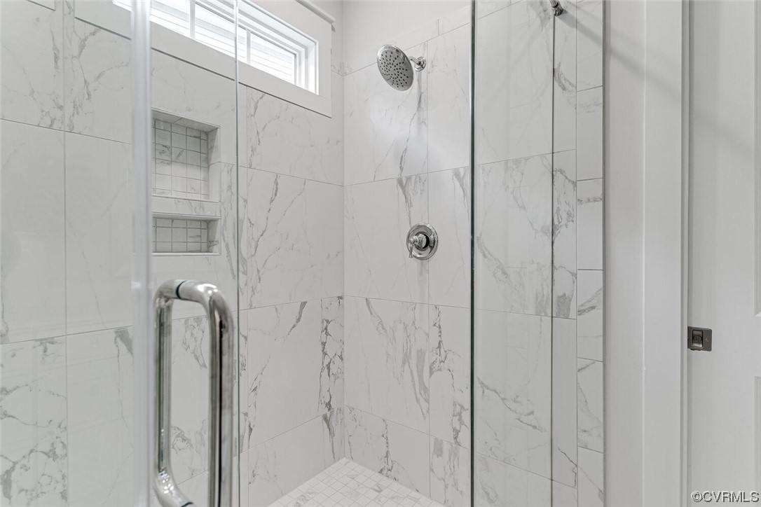 Walk-in shower with white marble-look tile, glass enclosure, built-in niche, and a high window.