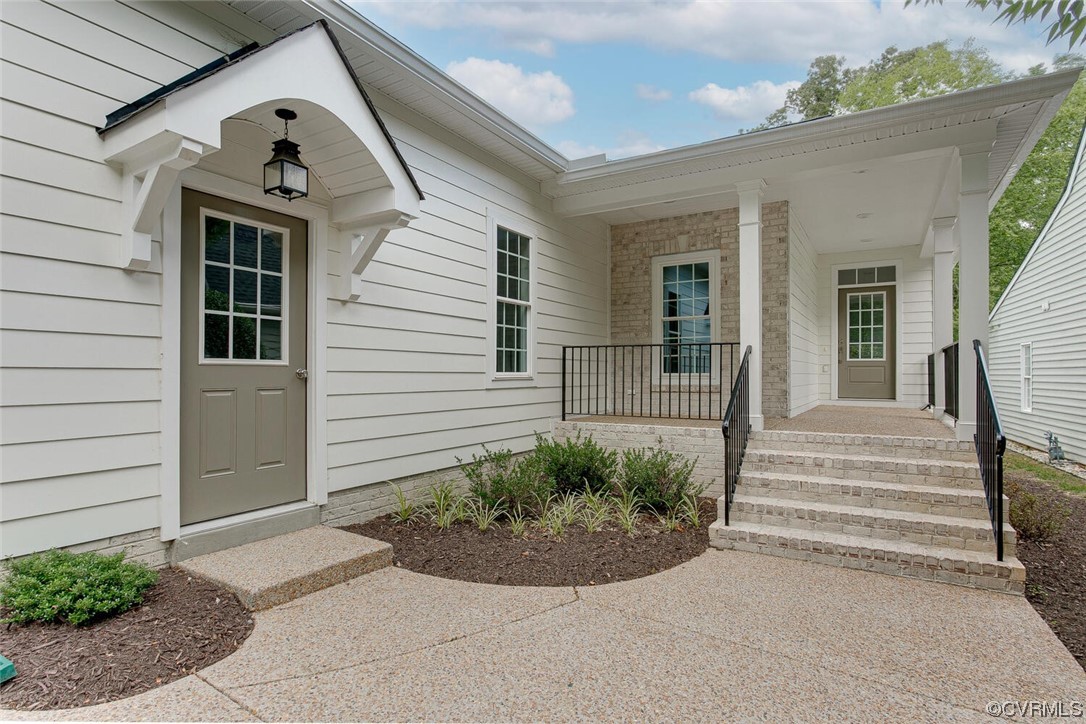 Home entrance with a covered porch, brick steps, black railings, and landscaped beds.