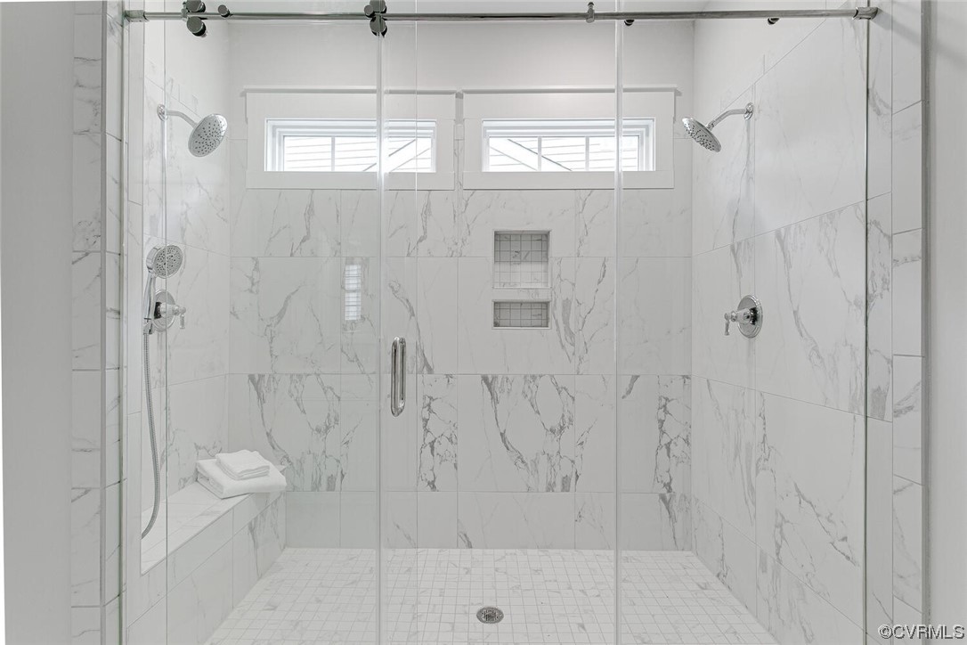 Walk-in shower with marble-look tile, dual showerheads, a built-in bench, and high windows.