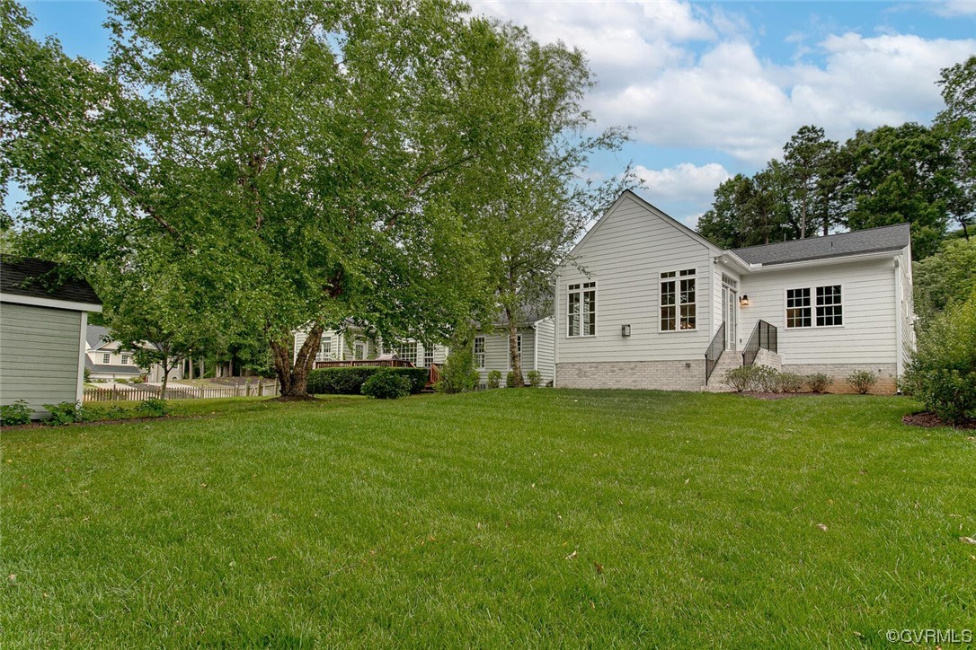 Rear of a white house beyond a broad lawn, shaded by mature leafy trees.