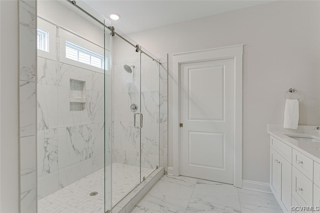 Bathroom with a glass-enclosed marble-look shower, high windows, and white vanity.