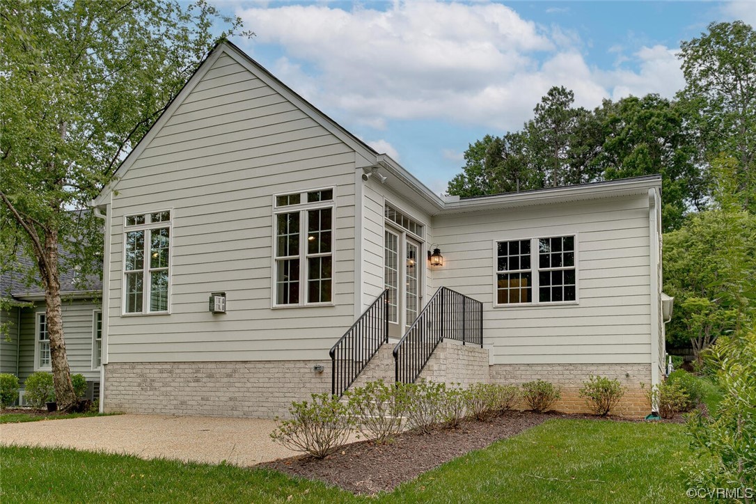 Light-sided home with a brick foundation, raised entry steps, black railings, and a gravel driveway.