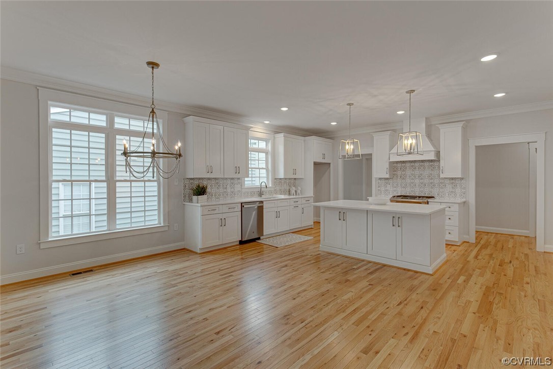 Vacant white kitchen with a large island, patterned tile backsplash, and light hardwood floors.