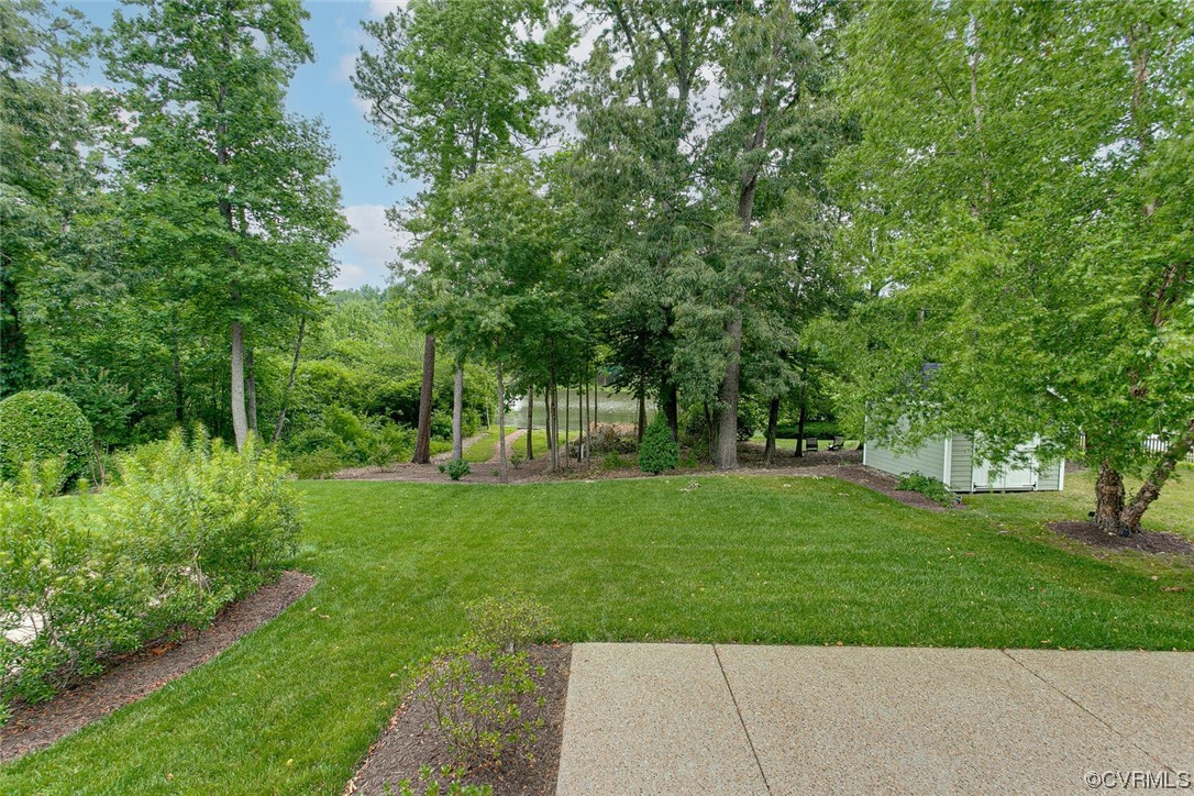 Backyard lawn bordered by mature trees and garden beds, with a white shed and concrete patio.