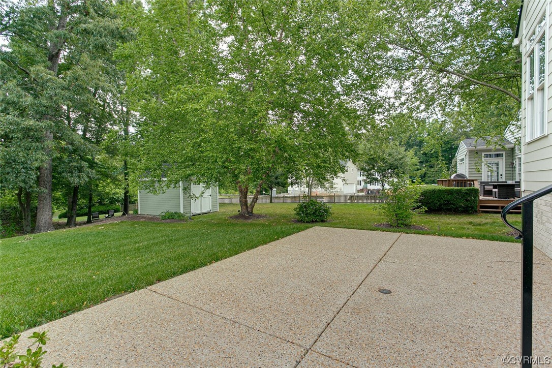 Concrete patio opening onto a tree-shaded backyard with a small shed.