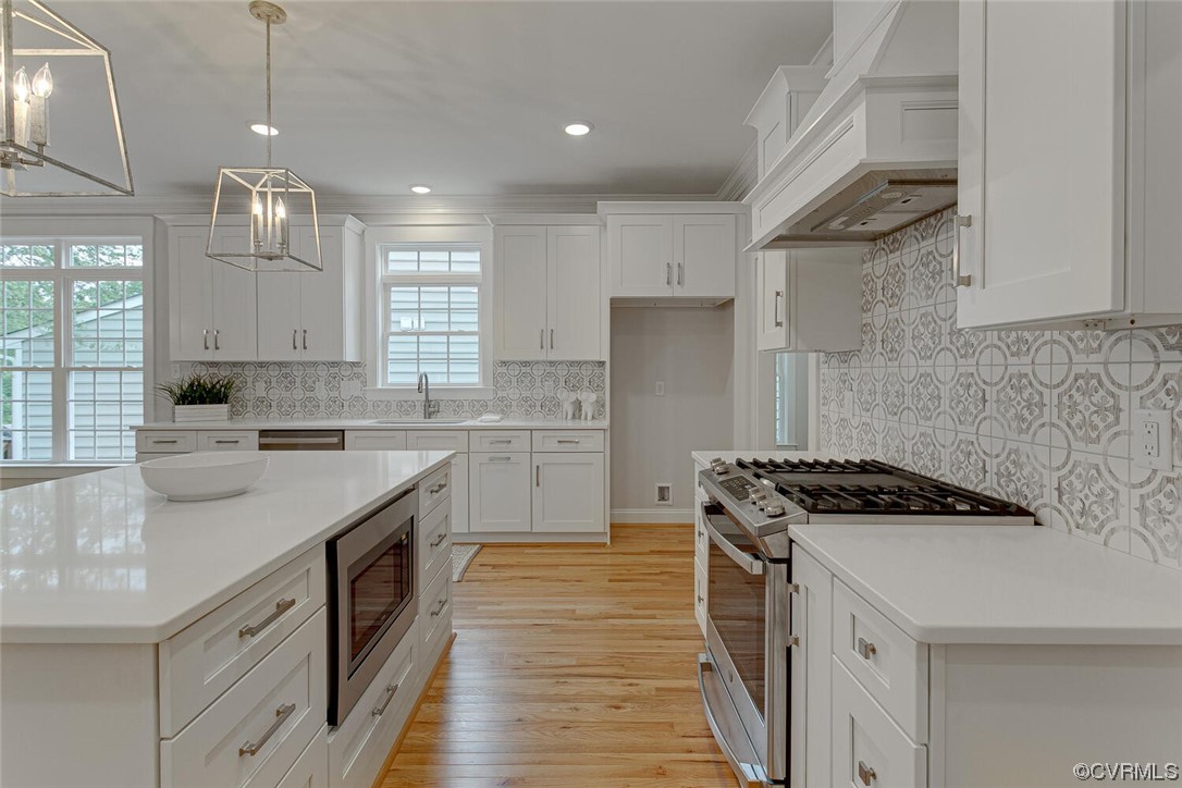 White kitchen with a large island, stainless steel gas range, patterned tile backsplash, and hardwood floors.