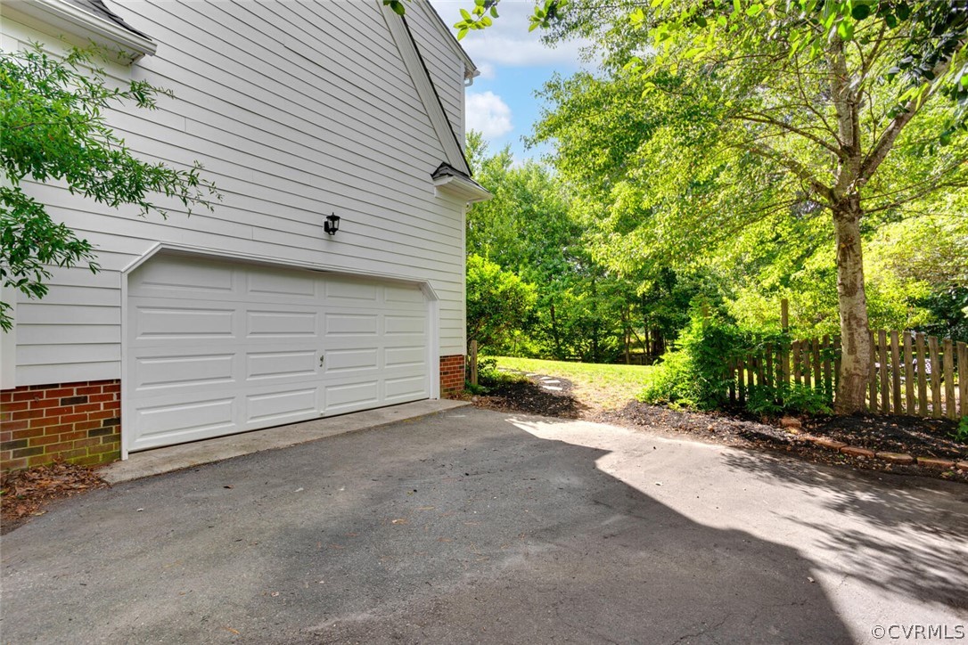 Home exterior with a double garage and paved driveway beside mature trees and a wooden fence.
