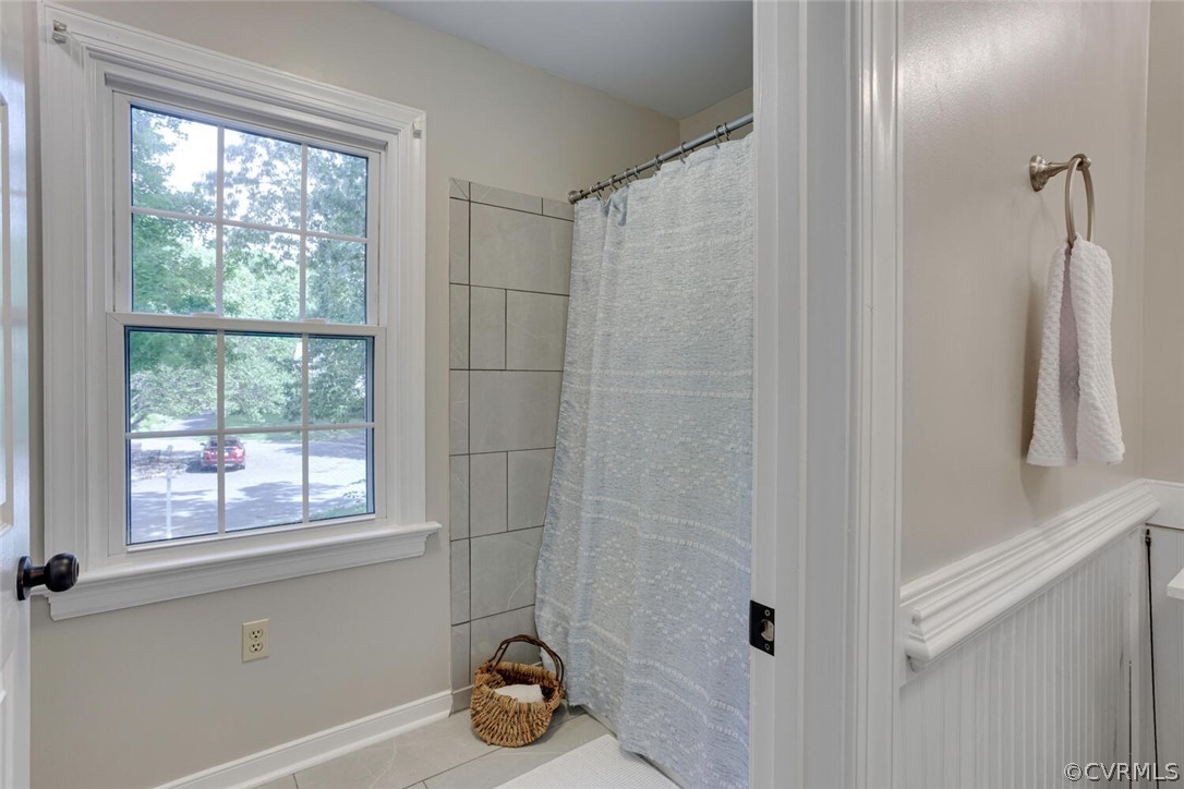 Bathroom with tiled shower, pale blue curtain, and large window overlooking trees.