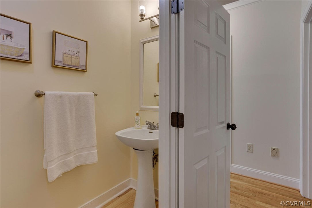 Bathroom with a pedestal sink, framed art, and towel beside an open door.