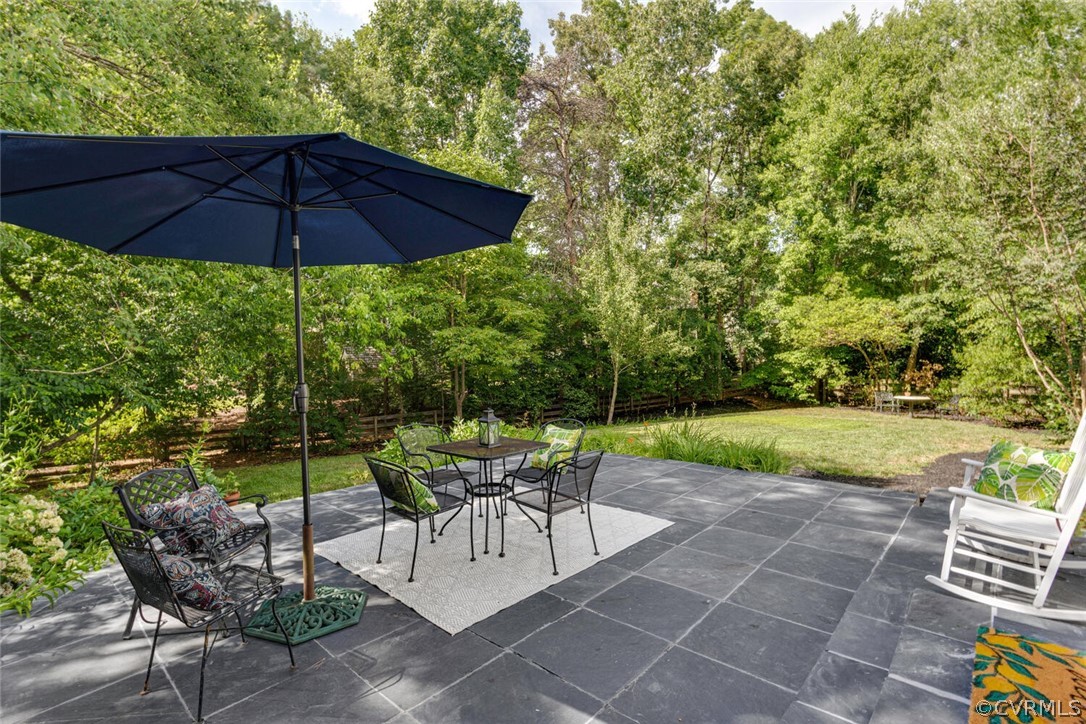 Stone patio with umbrella-covered dining set overlooking a tree-lined lawn.