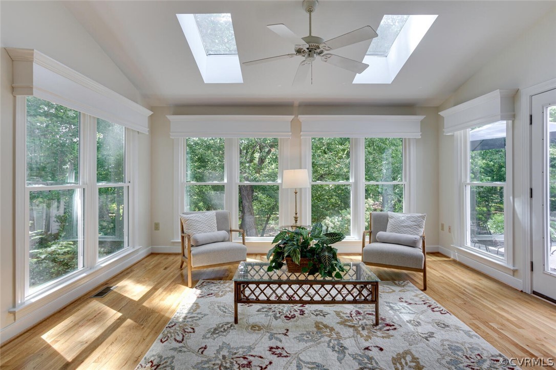 Sunroom with large windows, leafy views, two chairs, hardwood floors, and skylights.