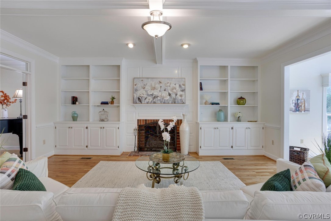 Living room with a brick fireplace, white built-ins, hardwood floors, and a glass coffee table.